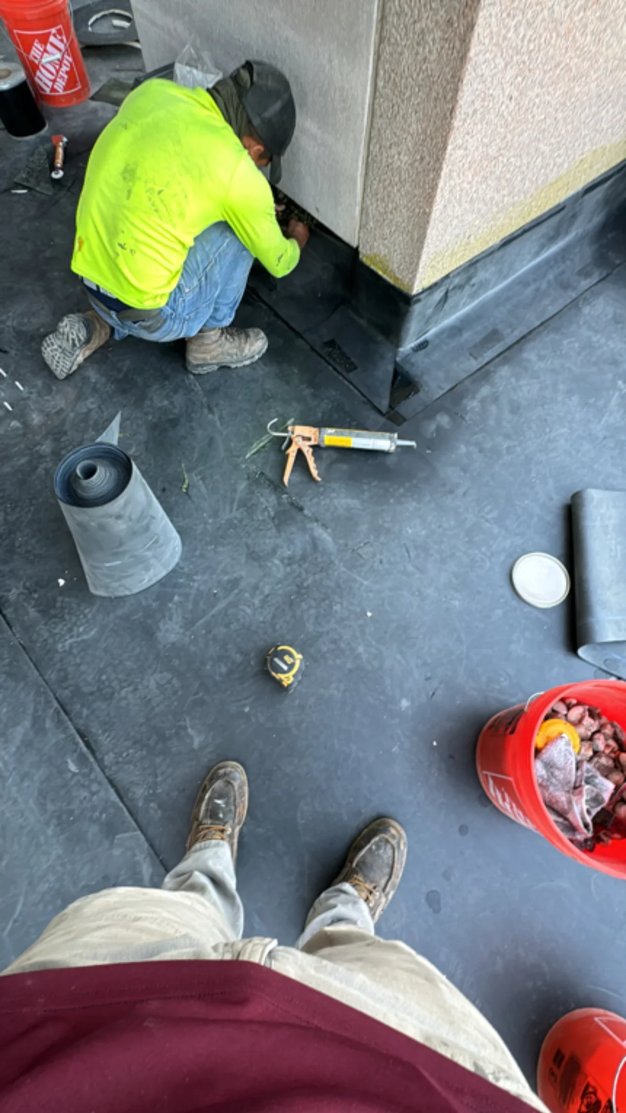 Worker installing black membrane roofing with sealant application at roof edge and wall transition
