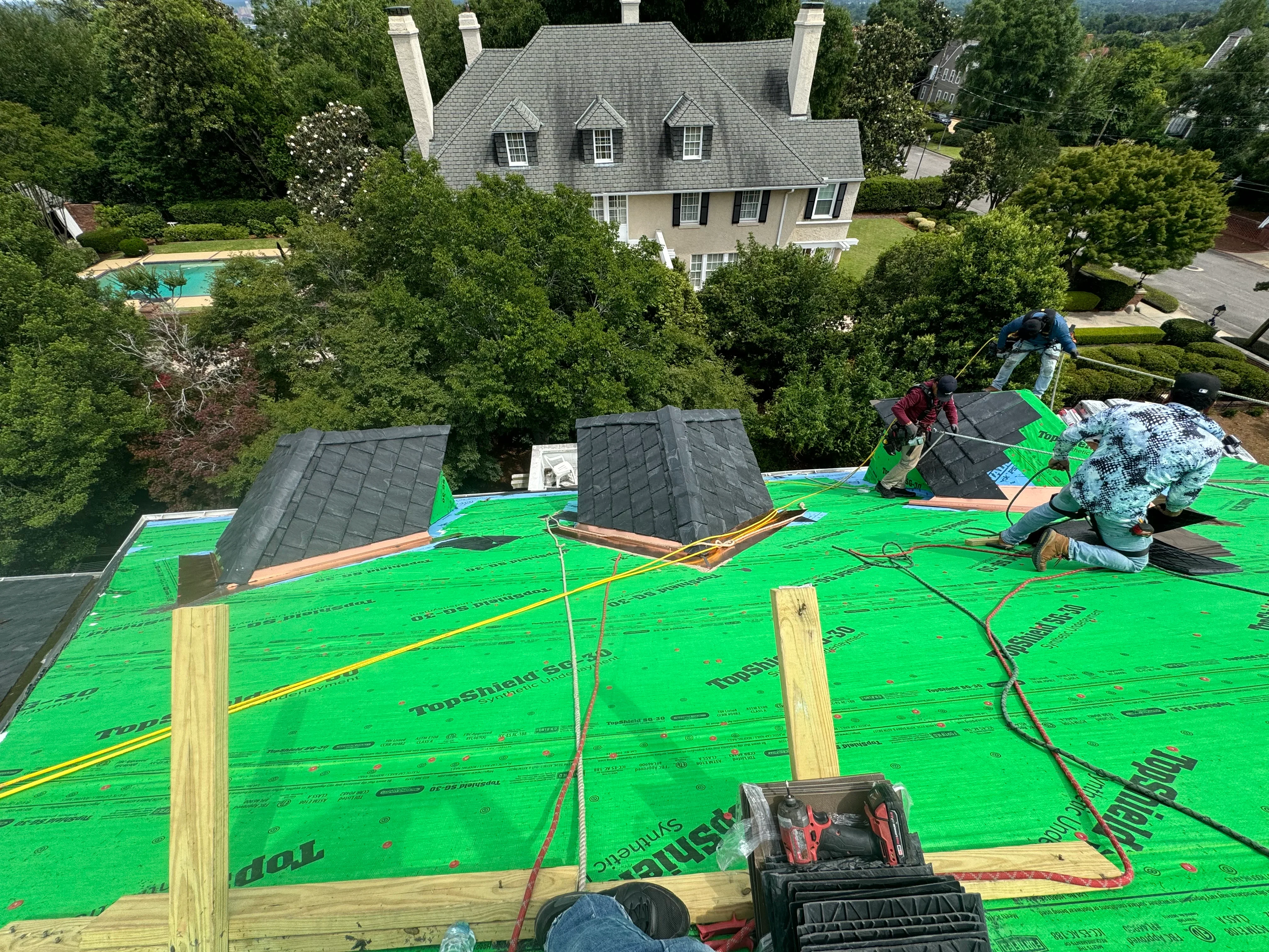 Roof installation with gray architectural shingles, green underlayment, and multiple roof planes on residential home