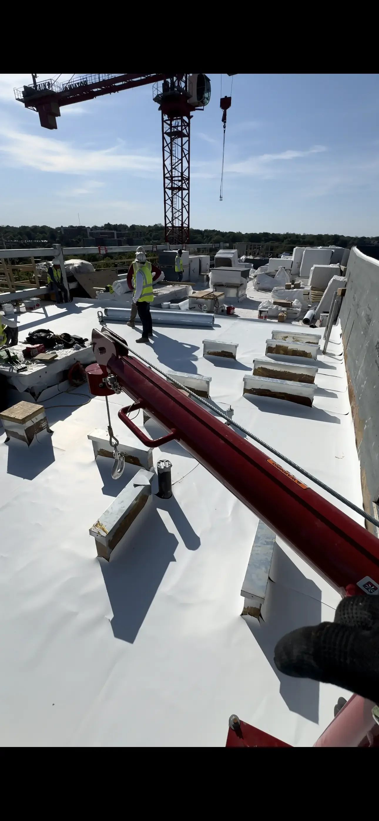 White membrane roofing installation on commercial flat roof with HVAC units and crane overhead