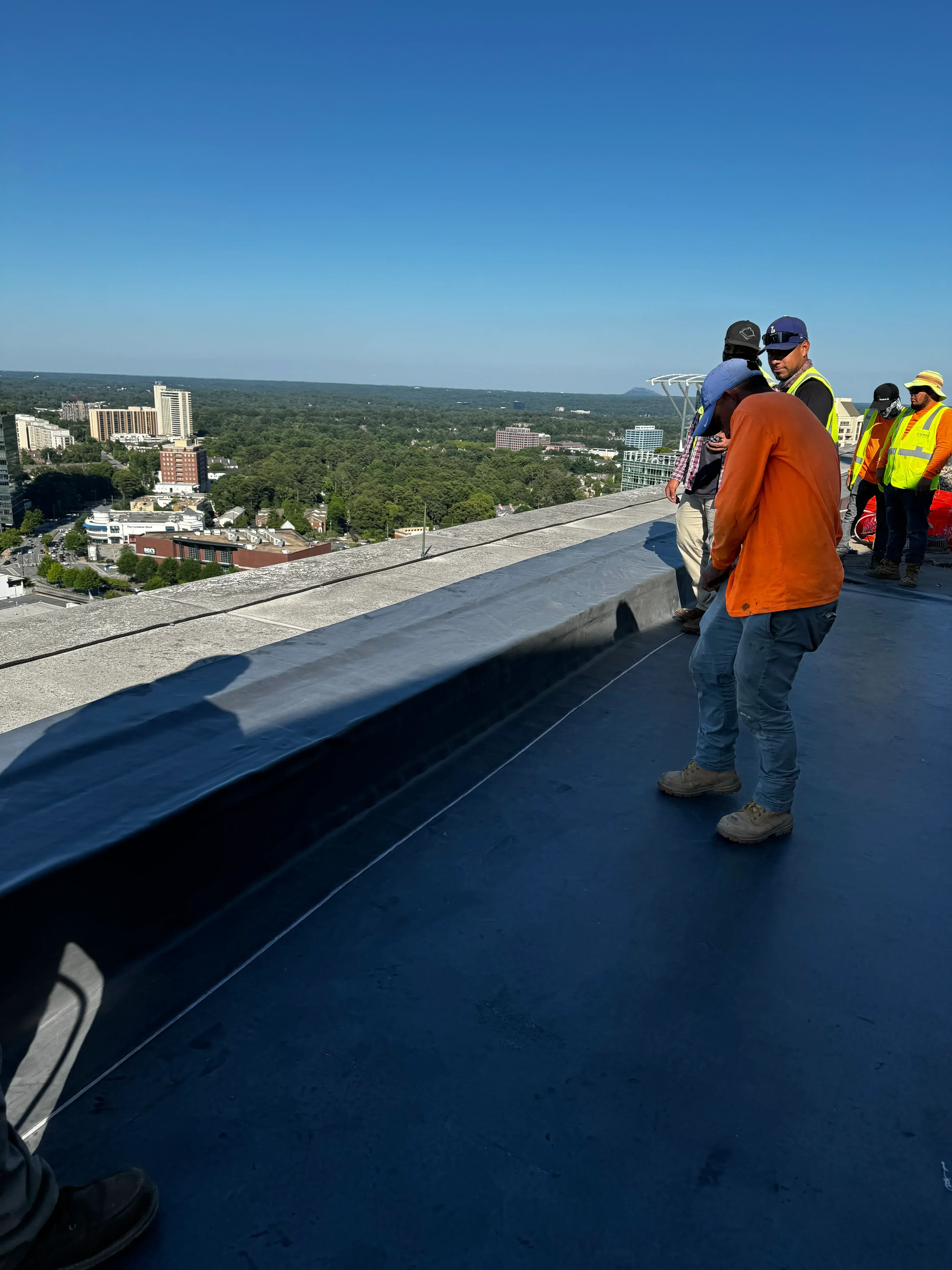 Roofer installing asphalt shingles on pitched residential roof with safety harness