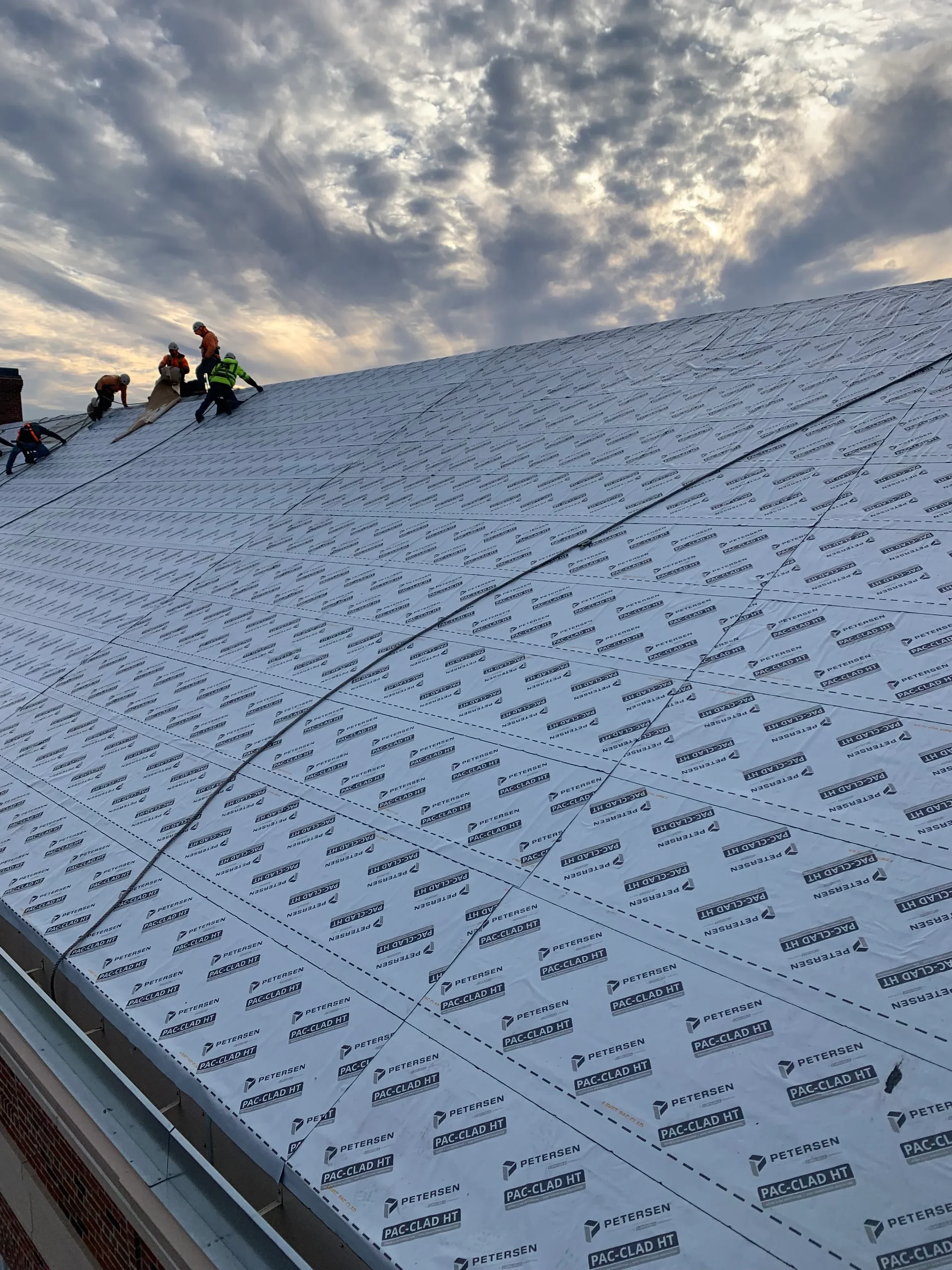 Roofers installing synthetic underlayment on steep pitched roof with safety harnesses