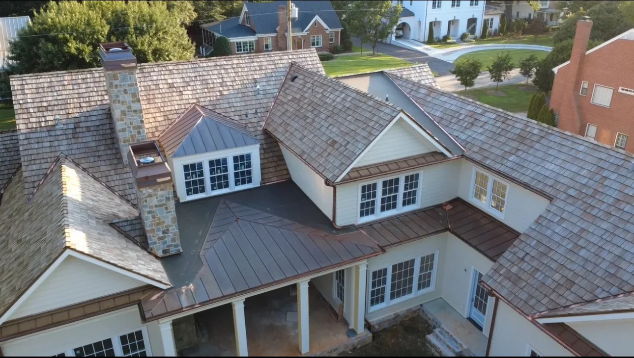 Standing seam metal roof and asphalt shingles on multi-level residential home with dormers and stone chimney